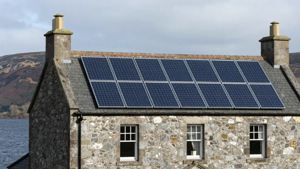 A traditional Scottish stone house with a black solar array on its slate roof beside a loch