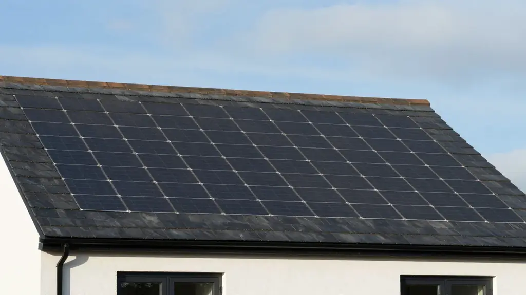 A modern white house with its whole dark roof covered in uniform solar roof tiles under a pale sky